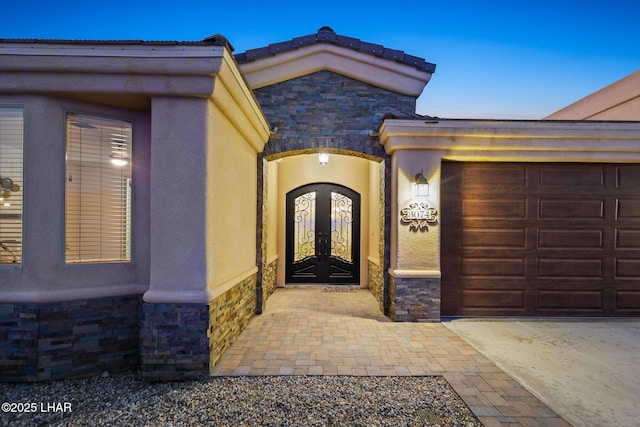 view of exterior entry with stone siding, stucco siding, french doors, and an attached garage