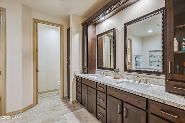 full bathroom featuring double vanity, wood finished floors, toilet, and a sink