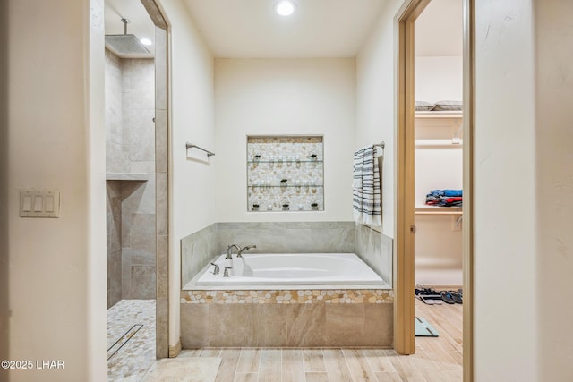 bathroom with tiled shower, a walk in closet, a garden tub, and wood finished floors