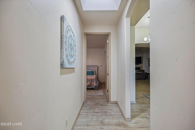 hallway with baseboards, a skylight, and light wood finished floors