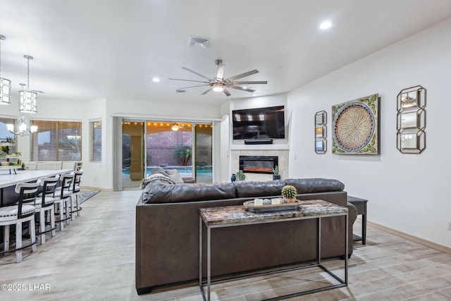 living room with visible vents, light wood-style flooring, recessed lighting, a tiled fireplace, and ceiling fan with notable chandelier