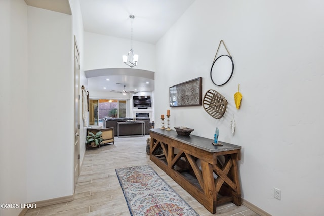 foyer featuring baseboards, wood tiled floor, a fireplace, arched walkways, and ceiling fan with notable chandelier