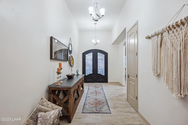 foyer with baseboards, wood tiled floor, arched walkways, french doors, and a chandelier