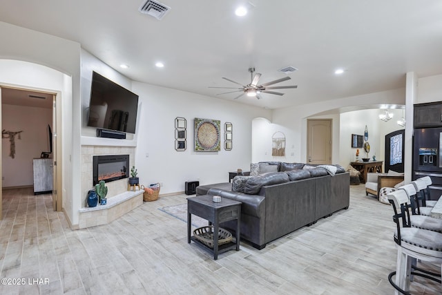 living area with visible vents, light wood finished floors, a fireplace, arched walkways, and ceiling fan