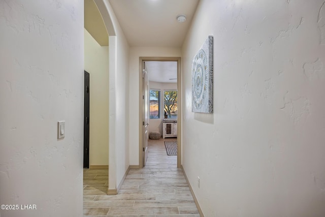 corridor with baseboards and light wood-style flooring