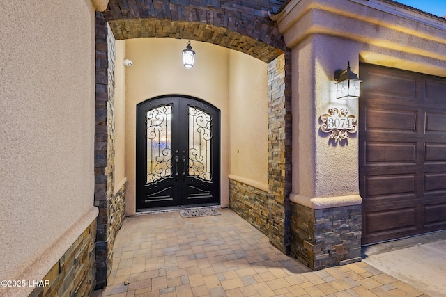 view of exterior entry featuring stone siding, stucco siding, and french doors