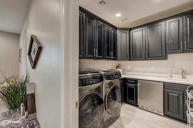 washroom with visible vents, washer and dryer, a sink, cabinet space, and light wood-style flooring
