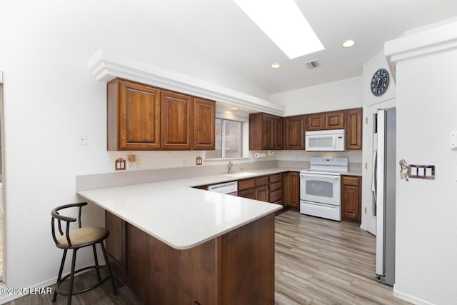 kitchen with vaulted ceiling with skylight, a kitchen breakfast bar, white appliances, light countertops, and a peninsula
