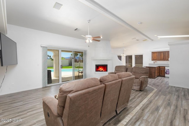 living area with light wood-type flooring, vaulted ceiling with beams, a fireplace, and ceiling fan