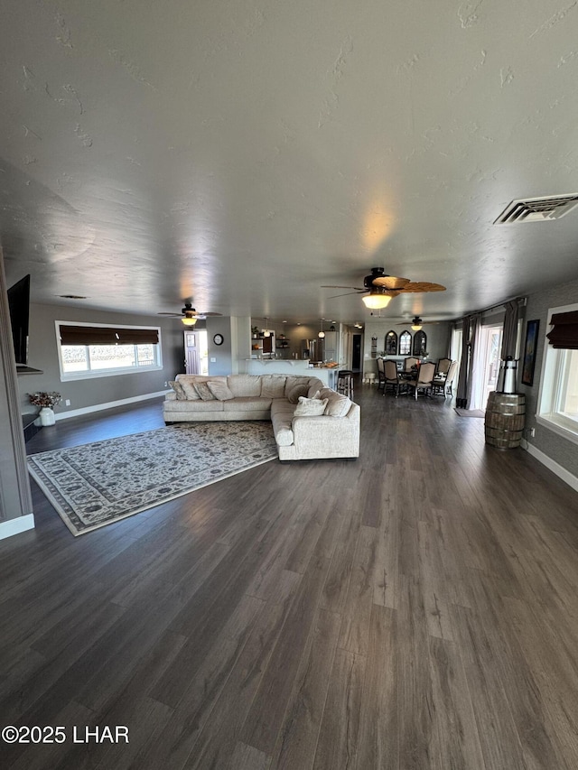 unfurnished living room with baseboards, visible vents, ceiling fan, dark wood-style flooring, and a textured ceiling