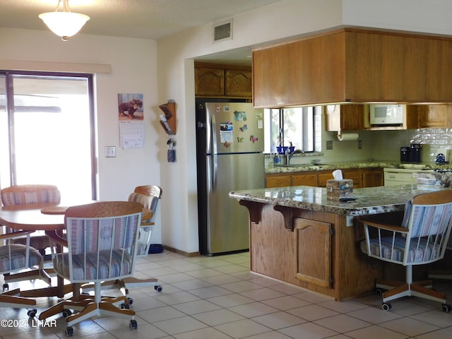 kitchen with light stone counters, sink, stainless steel refrigerator, and light tile patterned flooring