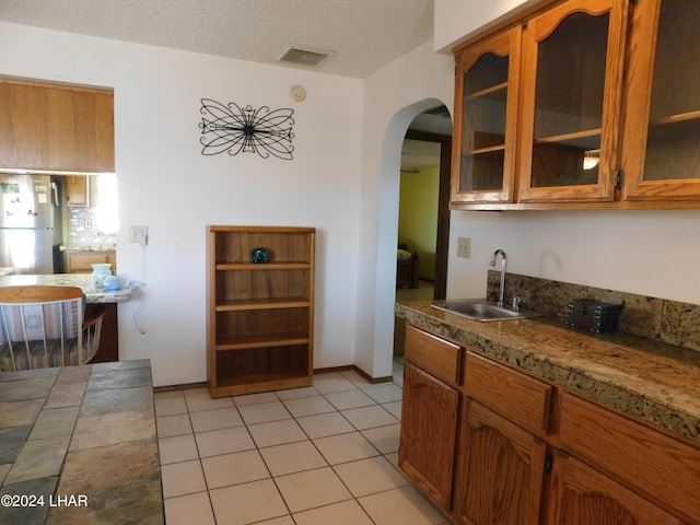 kitchen featuring light tile patterned flooring, sink, stainless steel fridge, and a textured ceiling