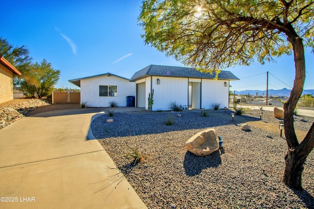 view of front of property with driveway, a shingled roof, an outdoor structure, and fence