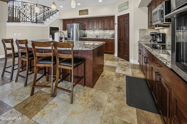 8652 Hopi Dr, Parker, AZ 85344 - kitchen with appliances with stainless steel finishes, decorative backsplash, a center island with sink, a breakfast bar area, and decorative light fixtures