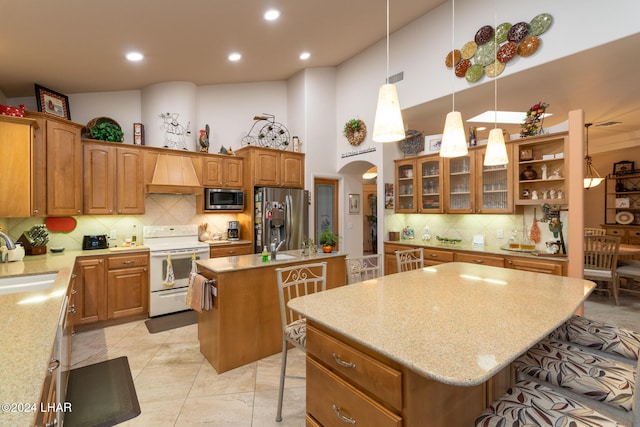 kitchen with arched walkways, custom range hood, appliances with stainless steel finishes, a sink, and an island with sink