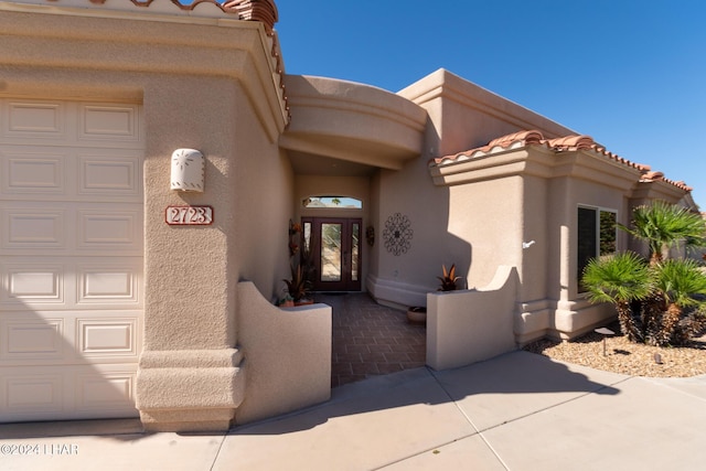 view of exterior entry featuring a tiled roof, an attached garage, and stucco siding