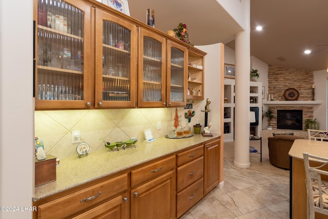 kitchen with a stone fireplace, light stone counters, open floor plan, backsplash, and glass insert cabinets