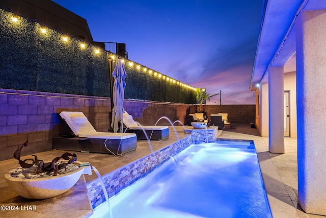 pool at dusk featuring pool water feature, a patio area, and an outdoor fire pit