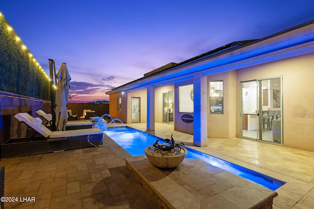 pool at dusk featuring a patio and pool water feature