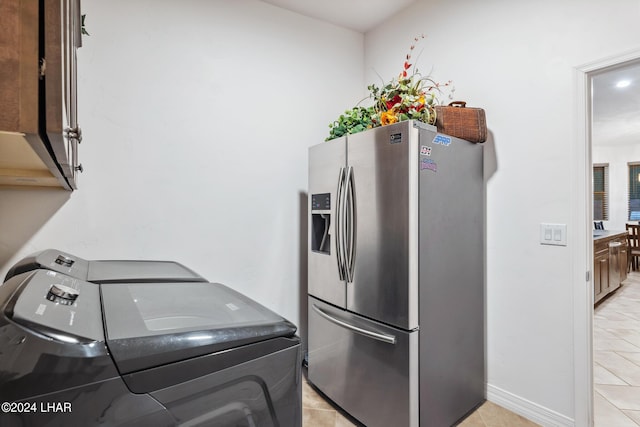 kitchen with light tile patterned flooring, dark brown cabinets, washing machine and clothes dryer, and stainless steel fridge