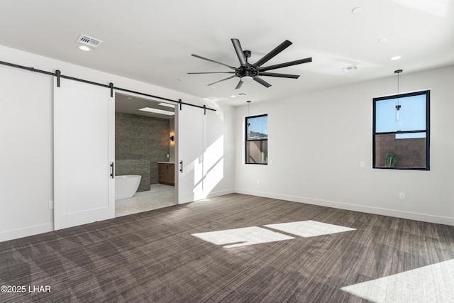 interior space with a barn door, dark carpet, and ensuite bath