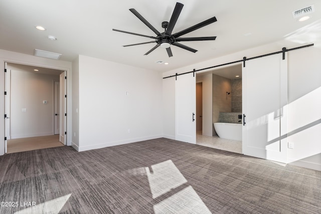 carpeted empty room with a barn door and ceiling fan