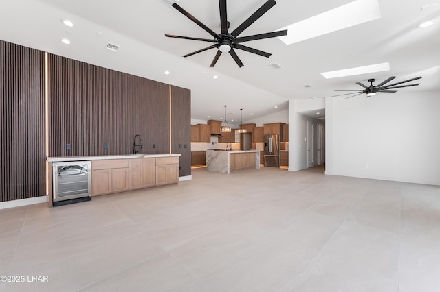 unfurnished living room with lofted ceiling with skylight, beverage cooler, and ceiling fan