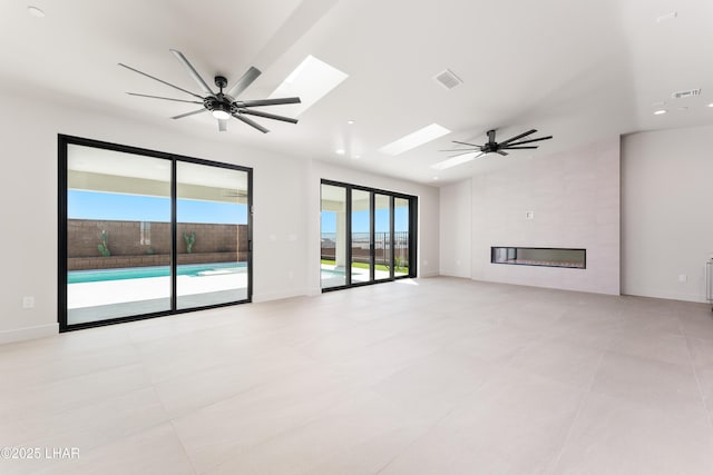 unfurnished living room with lofted ceiling with skylight, a large fireplace, and ceiling fan