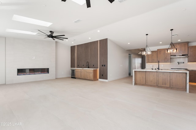 unfurnished living room featuring vaulted ceiling with skylight, sink, a large fireplace, ceiling fan, and beverage cooler