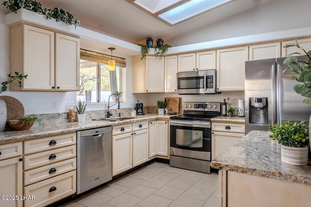 kitchen featuring light tile patterned floors, vaulted ceiling with skylight, a sink, appliances with stainless steel finishes, and cream cabinetry