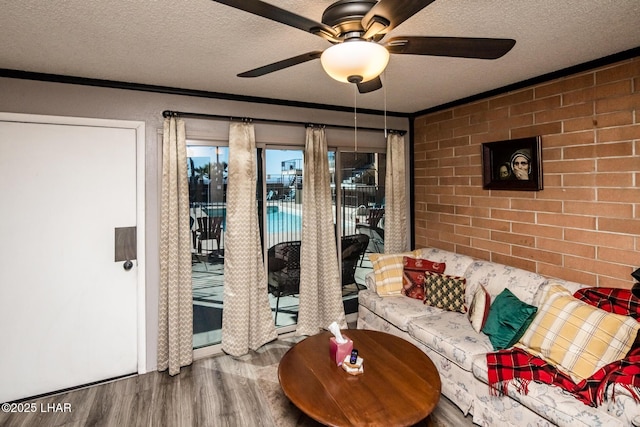 living room with ceiling fan, wood-type flooring, a textured ceiling, and brick wall