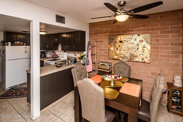 dining room featuring ceiling fan, brick wall, a textured ceiling, and light tile patterned flooring