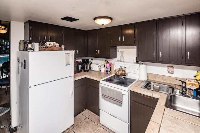 kitchen featuring light tile patterned floors, white appliances, sink, dark brown cabinets, and tile counters