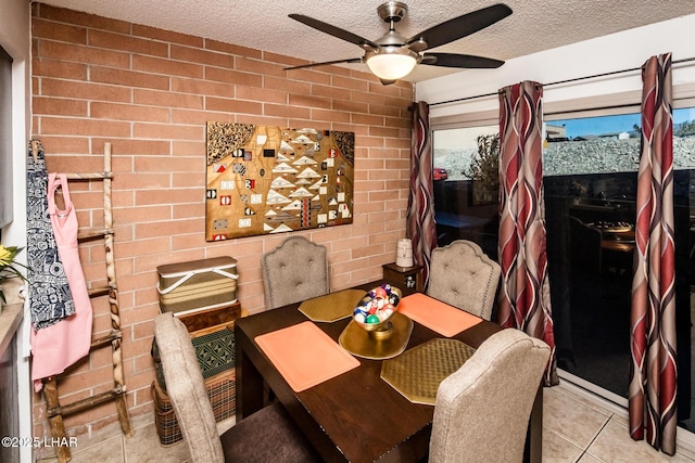 dining area featuring ceiling fan, brick wall, light tile patterned floors, and a textured ceiling