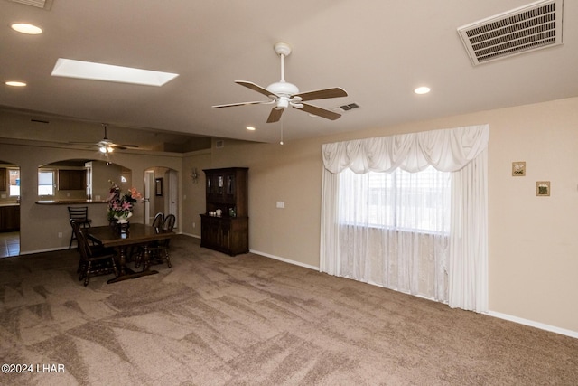 dining area featuring carpet floors, vaulted ceiling with skylight, and ceiling fan