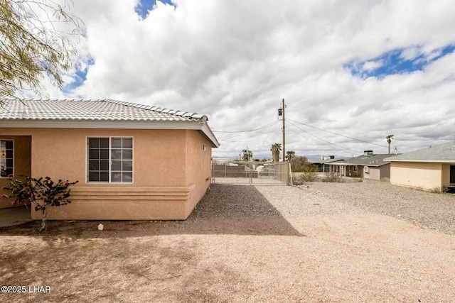 view of home's exterior with stucco siding, a tiled roof, fence, and a gate