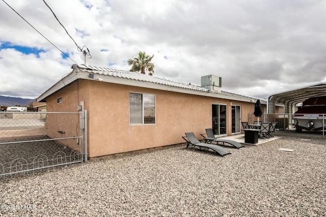 back of house with stucco siding, central air condition unit, a patio, fence, and a detached carport