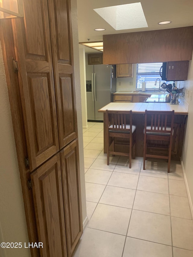 1008 Barcelona Unit 1, Lake Havasu City, AZ 86403 - kitchen with light tile patterned floors, a skylight, stainless steel refrigerator with ice dispenser, tile countertops, and recessed lighting
