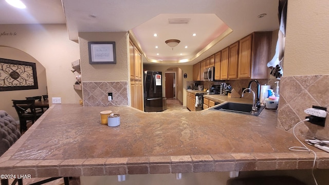 kitchen with sink, a breakfast bar area, a tray ceiling, black appliances, and kitchen peninsula