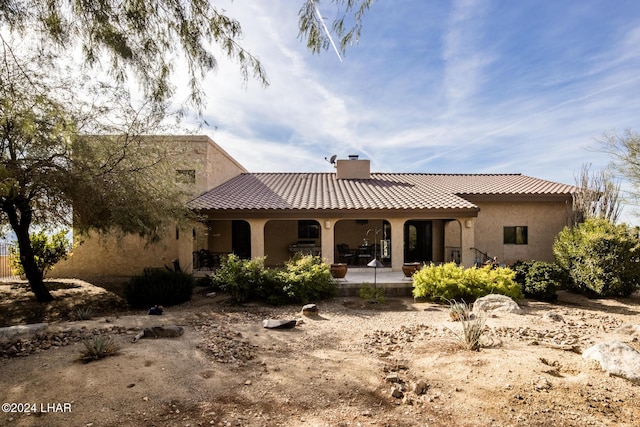 back of property with a chimney, a tile roof, stucco siding, and a patio area