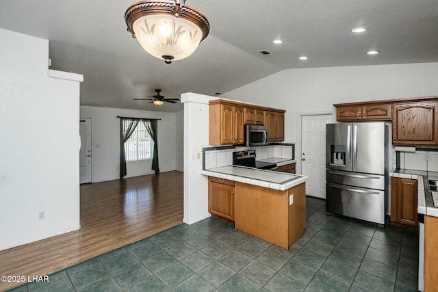 kitchen with a peninsula, dark tile patterned flooring, tile counters, appliances with stainless steel finishes, and open floor plan