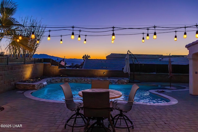 pool at dusk featuring pool water feature and a patio