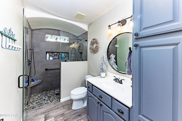 bathroom with tiled shower, toilet, wood-type flooring, a textured ceiling, and vanity