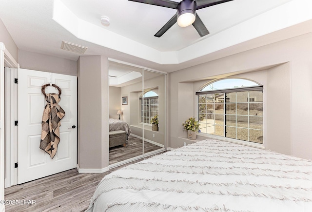 bedroom with a closet, hardwood / wood-style flooring, a raised ceiling, and ceiling fan