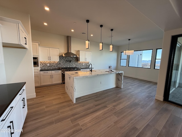 kitchen with pendant lighting, sink, white cabinets, stainless steel appliances, and wall chimney range hood