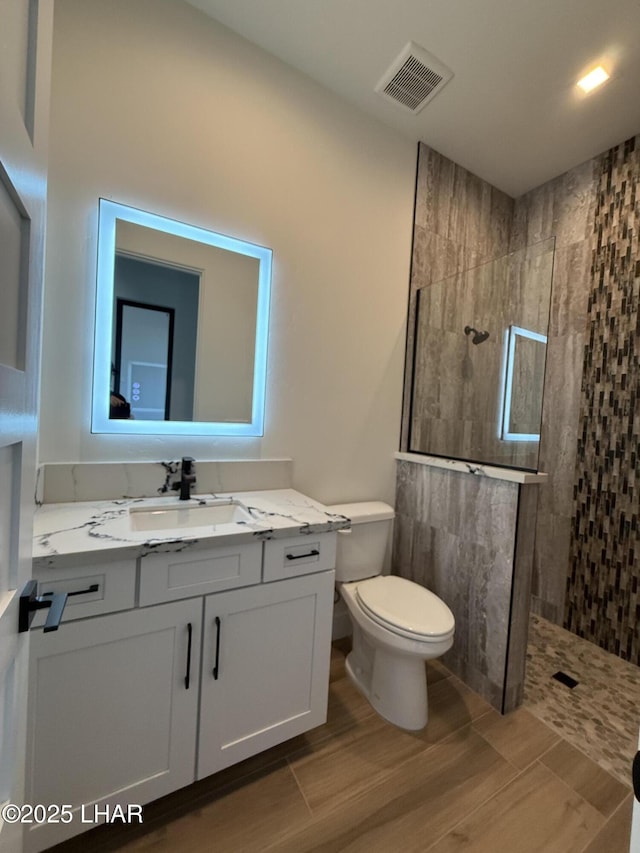 bathroom featuring vanity, a tile shower, and toilet