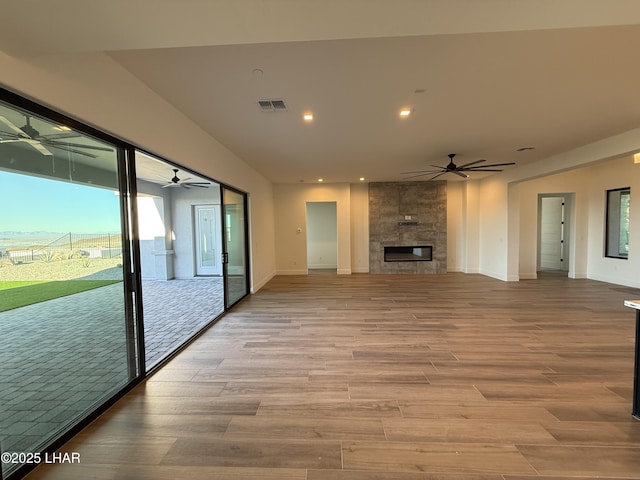 unfurnished living room featuring a tiled fireplace, plenty of natural light, ceiling fan, and light hardwood / wood-style flooring