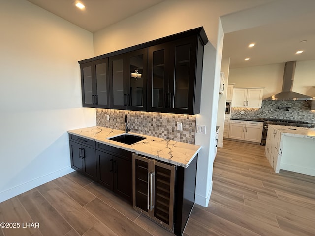 bar with white cabinetry, sink, beverage cooler, exhaust hood, and light stone countertops