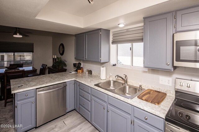 kitchen featuring sink, appliances with stainless steel finishes, gray cabinets, kitchen peninsula, and a raised ceiling