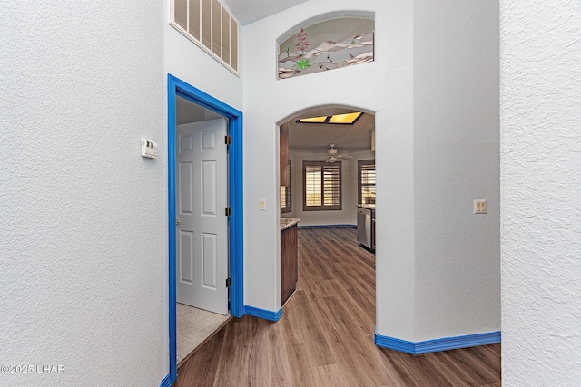 hall with arched walkways, visible vents, a textured wall, wood finished floors, and baseboards